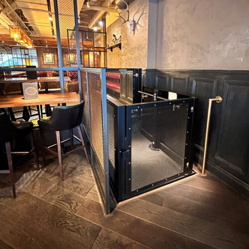 Compact, industrial-style platform lift with black mesh enclosure in a restaurant setting.
