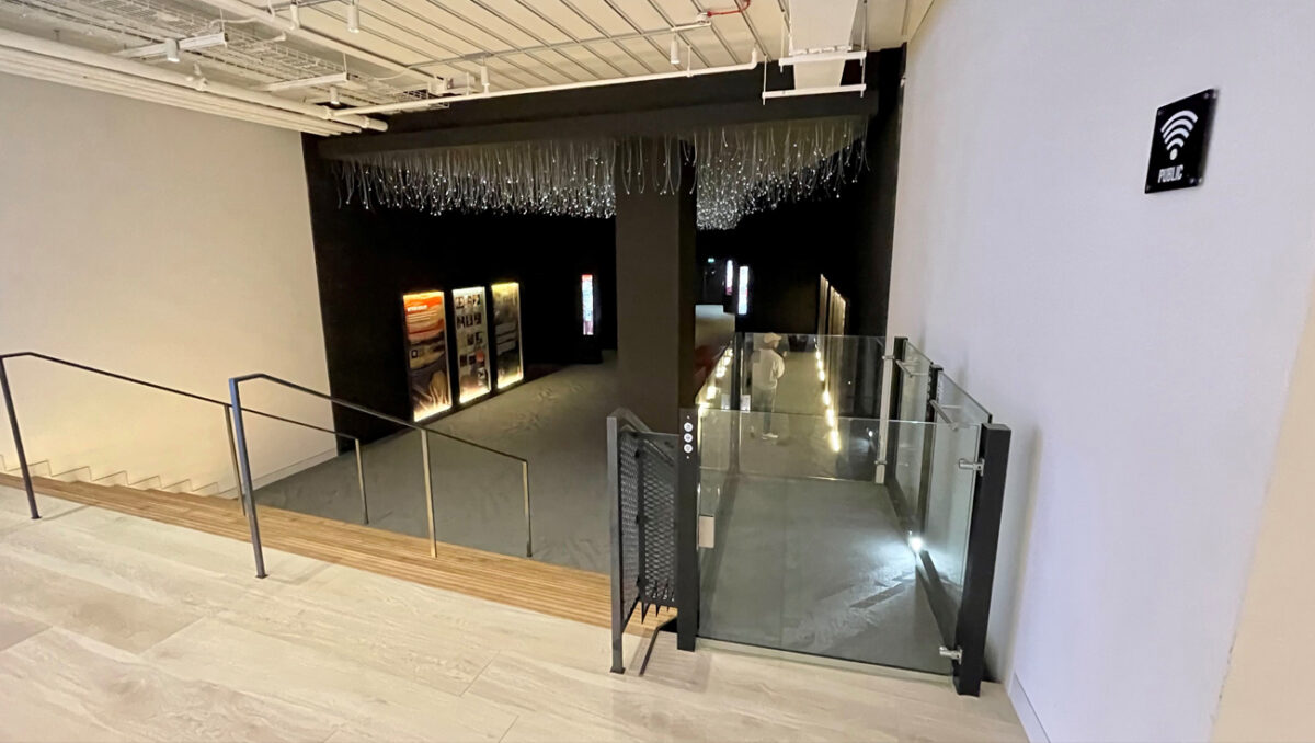 Stylish platform lift with glass enclosure descending into a modern, dark exhibition space.