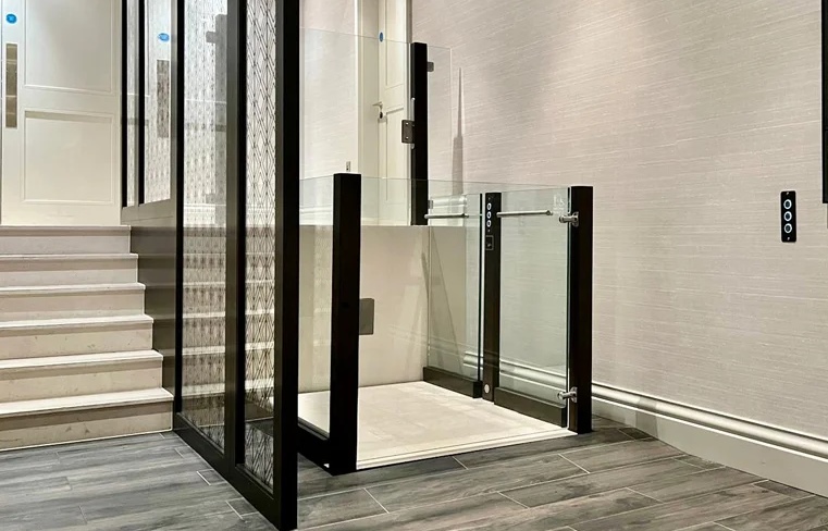Modern wheelchair lift with glass panels and dark frames next to a staircase.