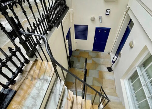 An exterior basement entrance with stone steps, black railings, and blue doors.